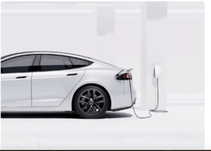 White electric car plugged into a wall charger in a bright minimalist garage setting seen from the rear side profile